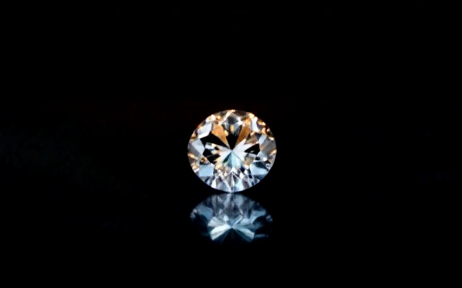 A loose round brilliant diamond on a dark reflective surface